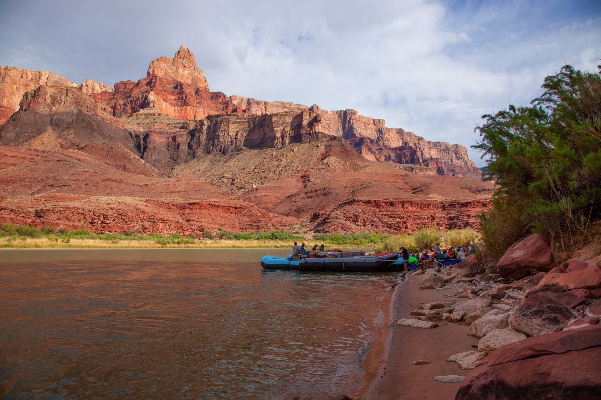 River raft on a sandy shore next to red rock cliffs.