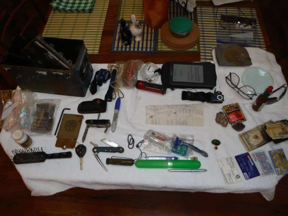 Items displayed on a white cloth on a wooden table: tools, money, electronics, and small objects.