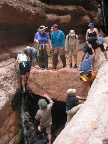 People hiking, climbing over a rock near a small waterfall in a canyon.