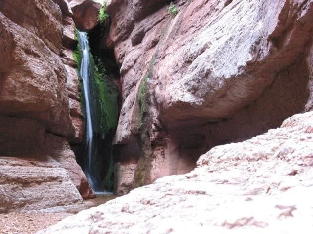 Waterfall cascading down a narrow red rock canyon.