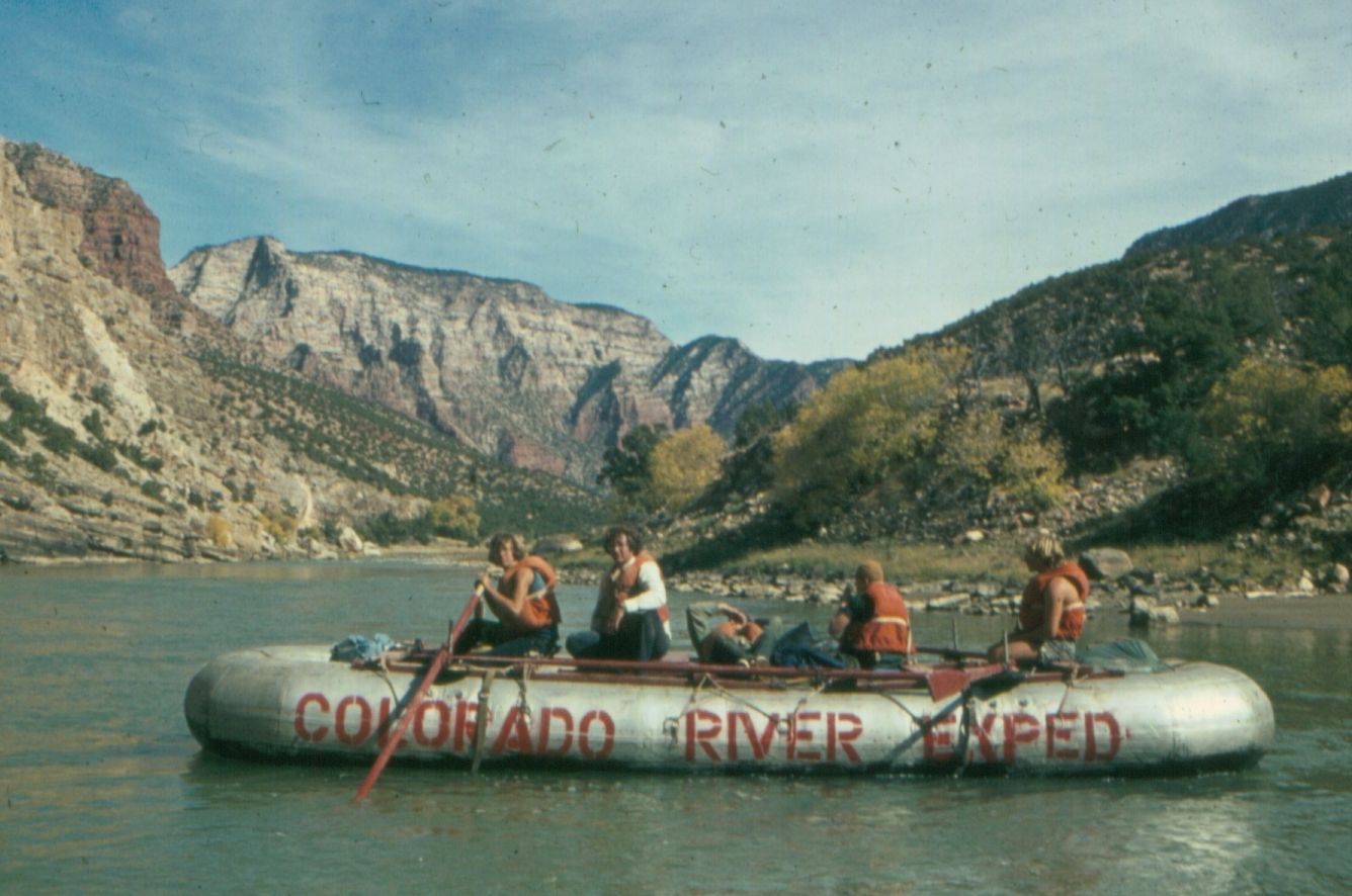 Raft on the Colorado River with passengers, mountains in the background.