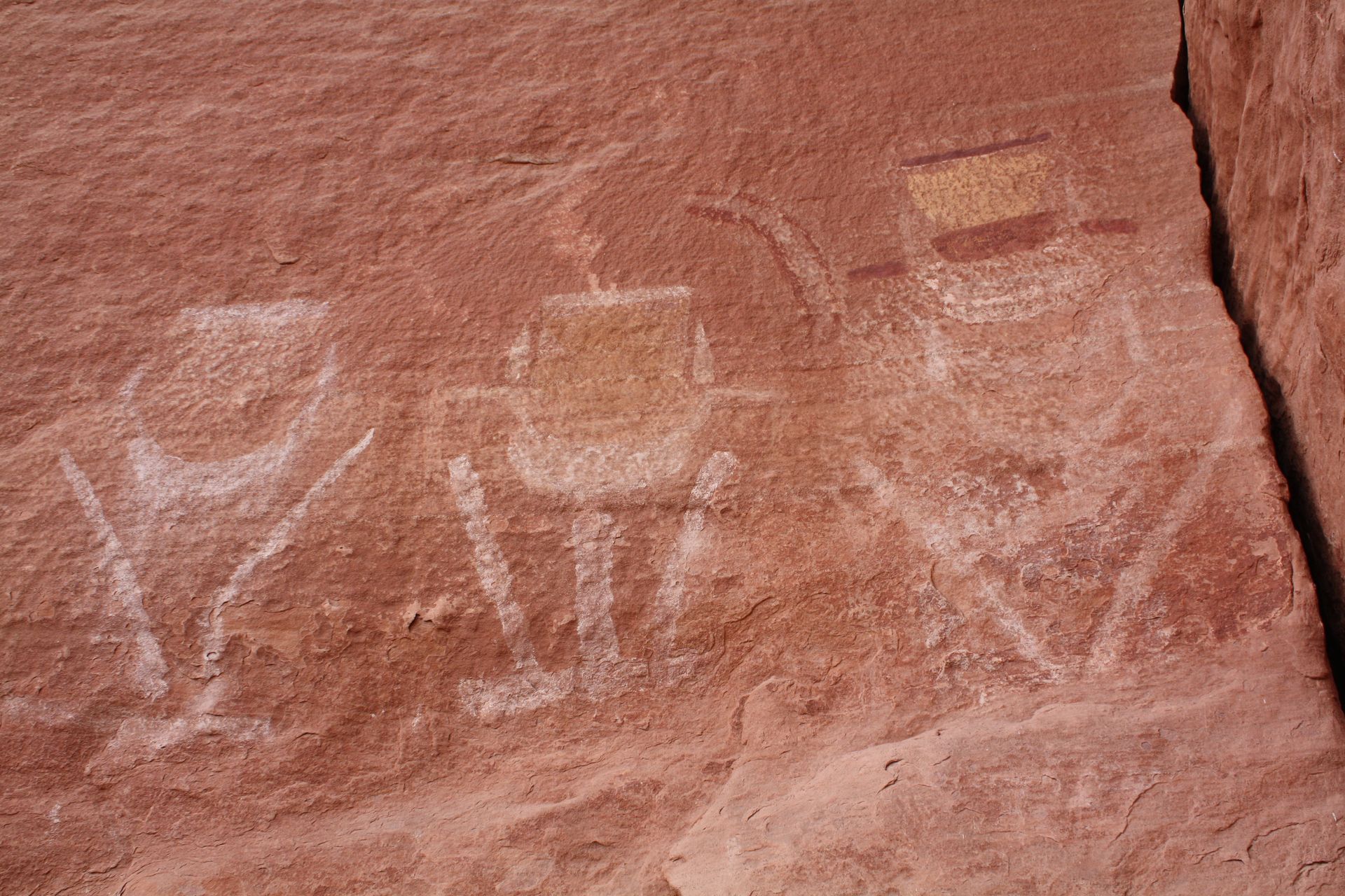 Three white figures with rectangular bodies and headgear are etched on red rock.