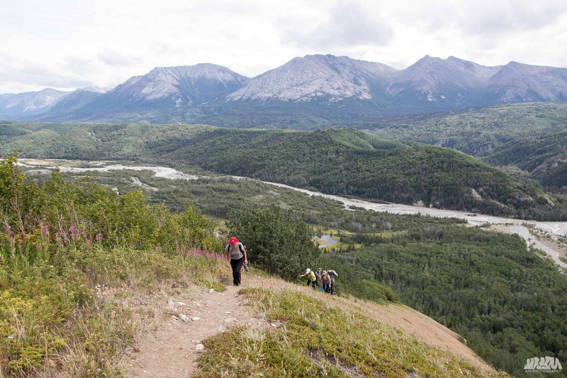 Hikers on a trail overlooking a river valley and mountains in Alaska.