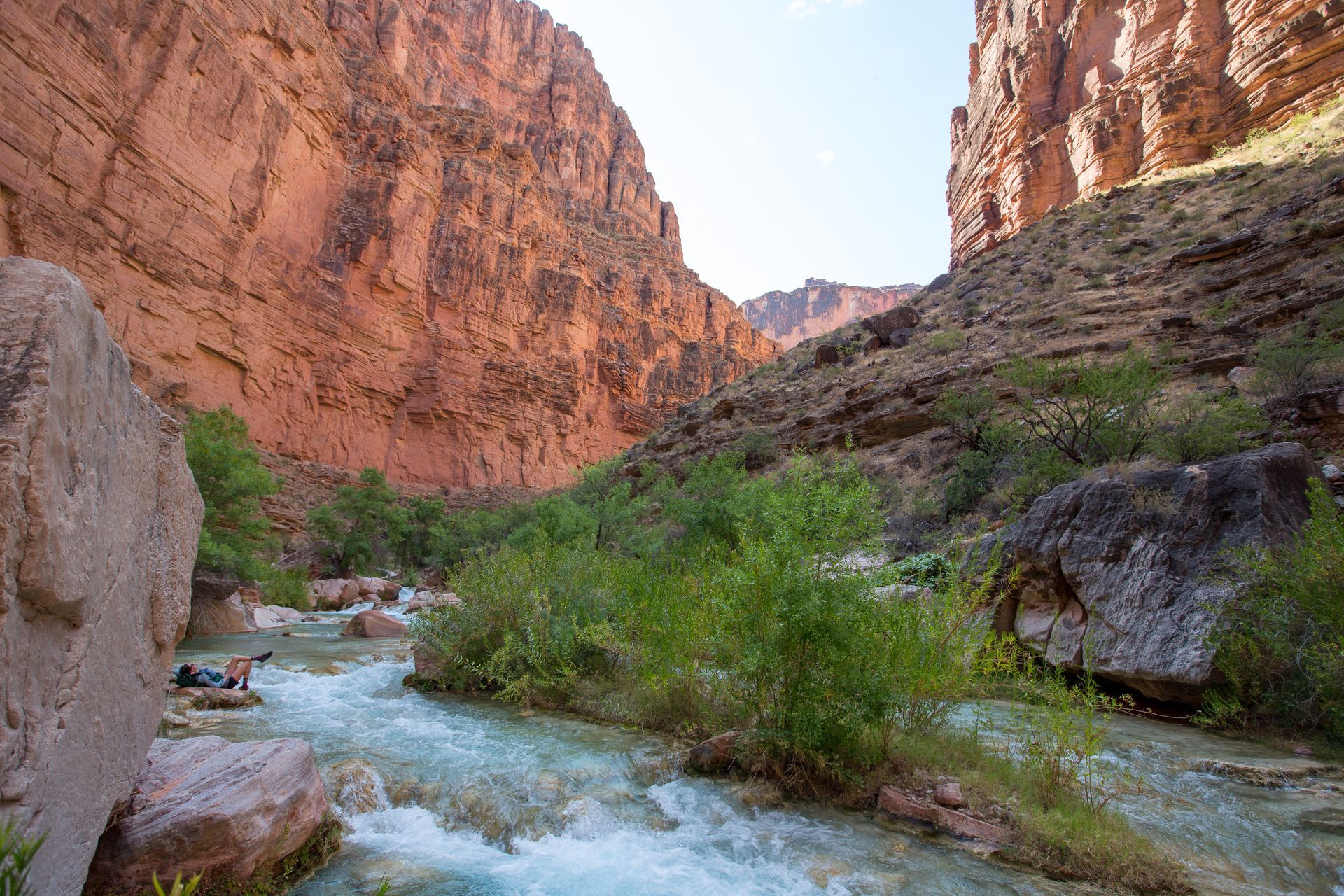 River flowing through a canyon with red rock walls and green vegetation.