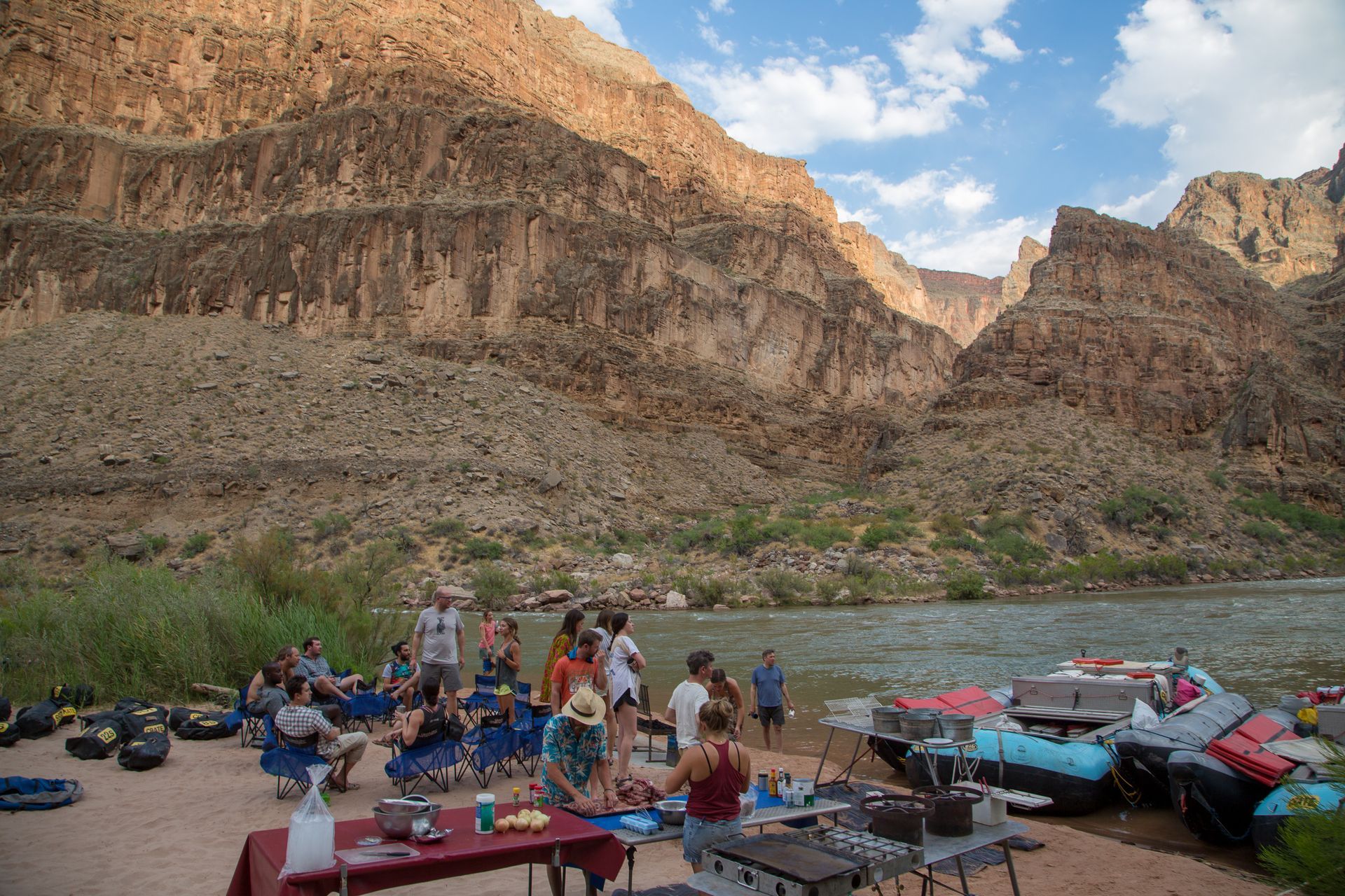 Group of people near river and rafts, canyon backdrop.