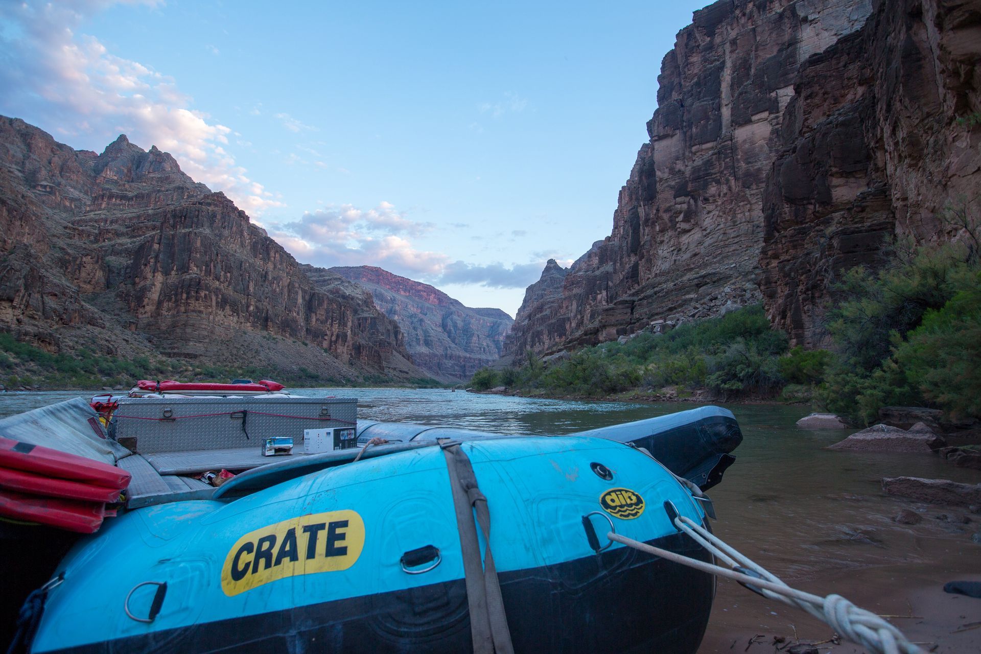 Blue raft tied to shore in a canyon river, surrounded by rock walls under a blue sky.