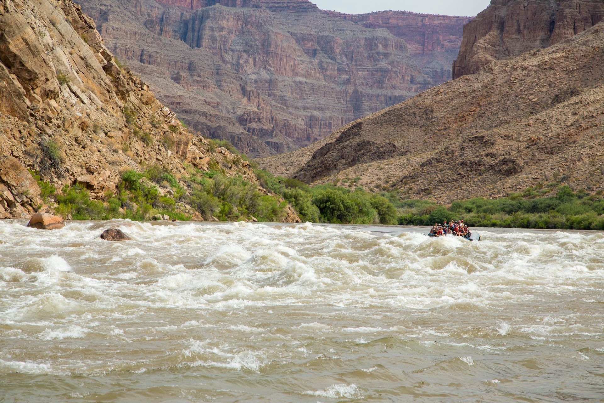 Whitewater rafting in a canyon, tan water, brown canyon walls.