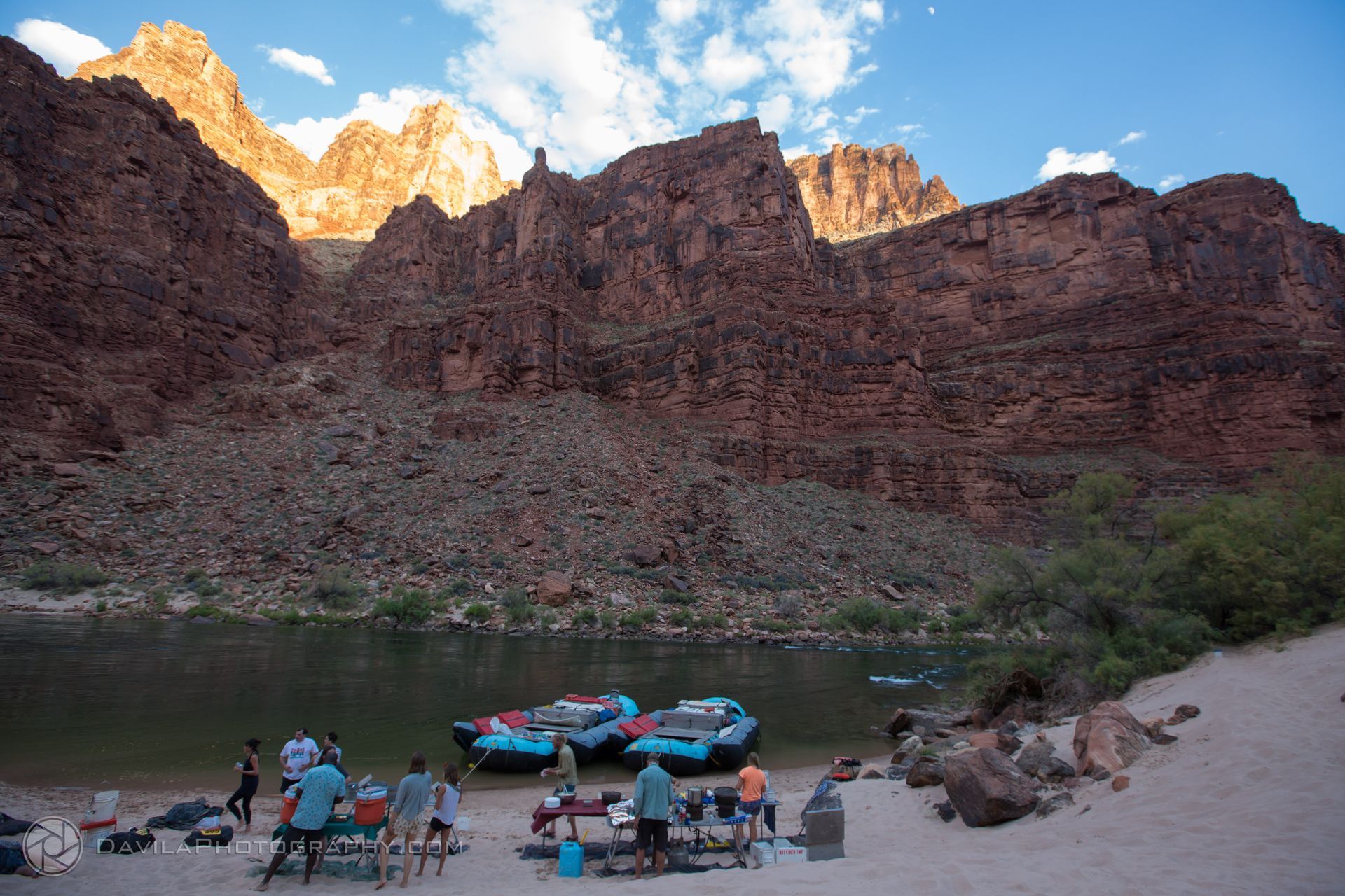 Rafting trip on a river with towering canyon walls. People gather on a sandy shore next to rafts.