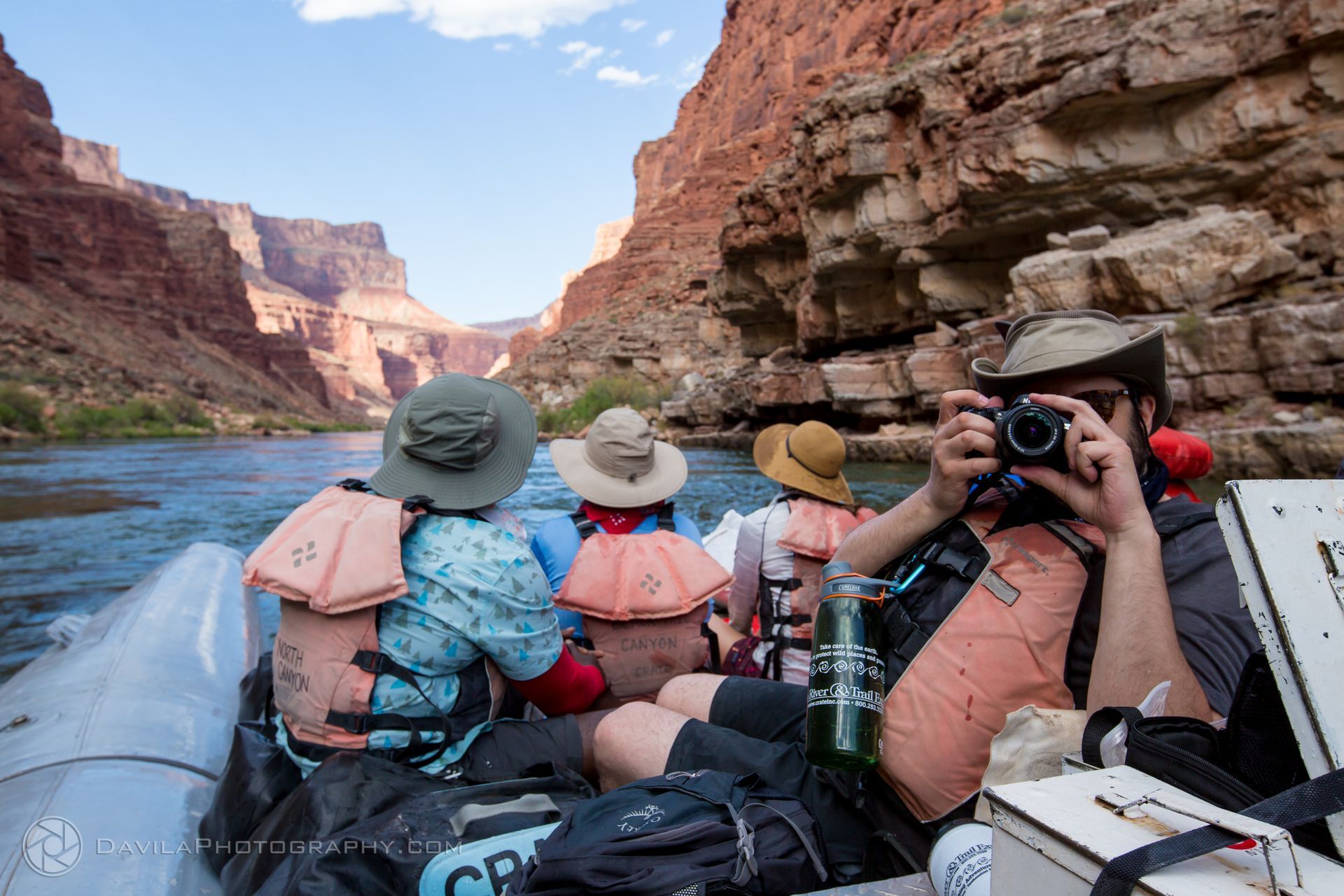 People in a raft on a river through a canyon, taking photos.