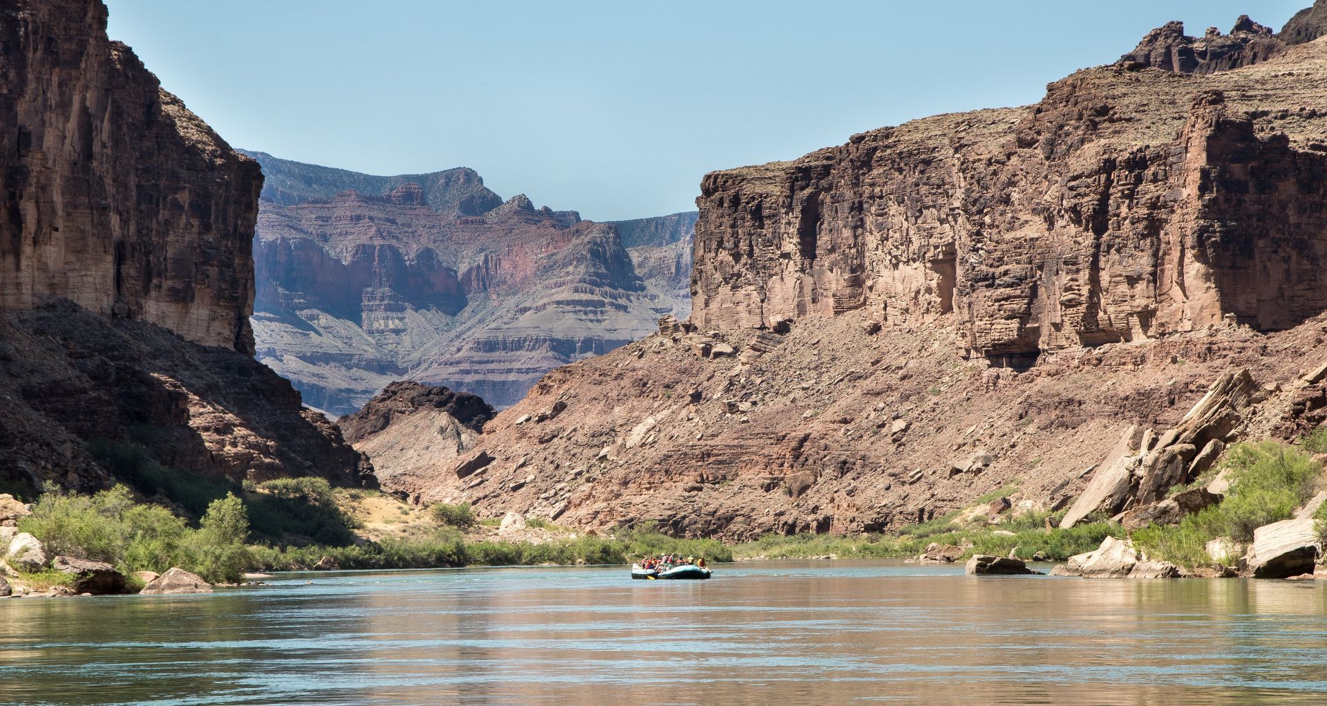 River flows between large rock formations. A boat with people navigates the water.