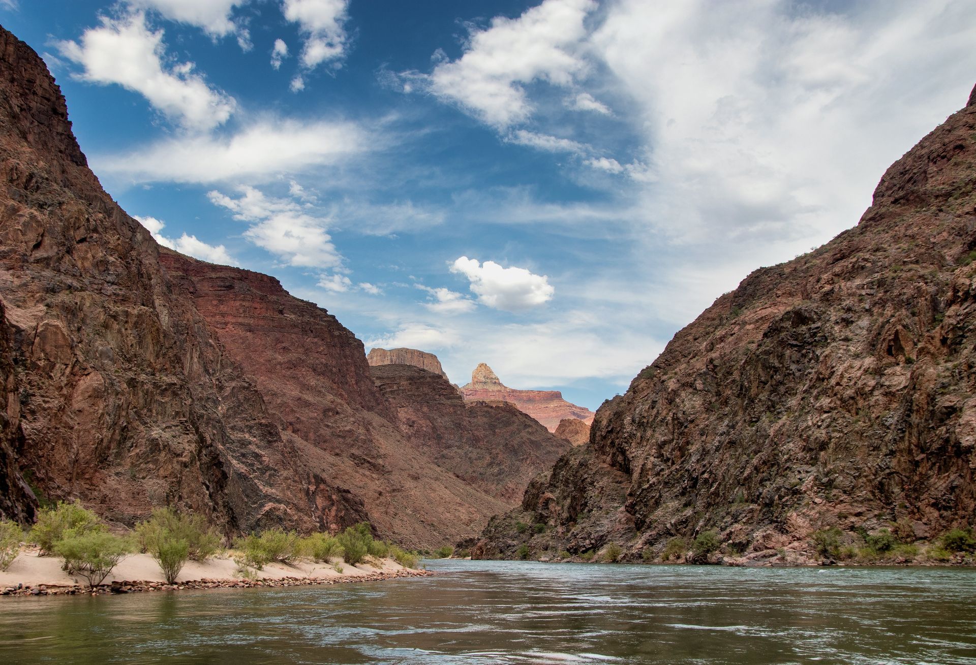 Canyon landscape with river. Red rock walls, blue sky with clouds, water flowing through canyon.