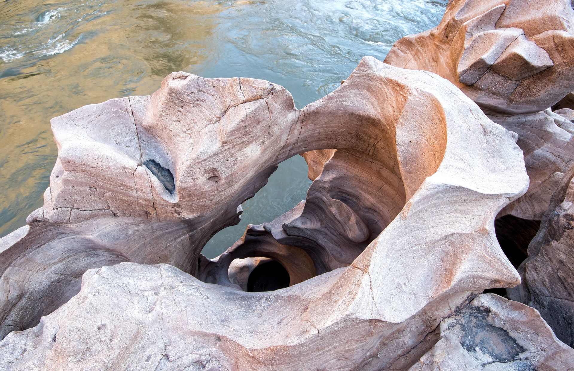 Eroded sandstone rock formations with archways, light and dark bands, near a flowing river.