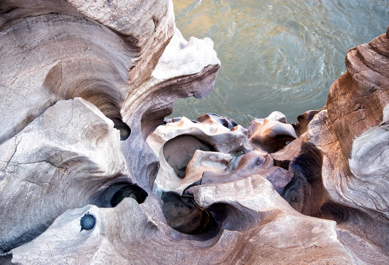 Eroded rock formations with swirling patterns border water, creating a natural, abstract landscape.