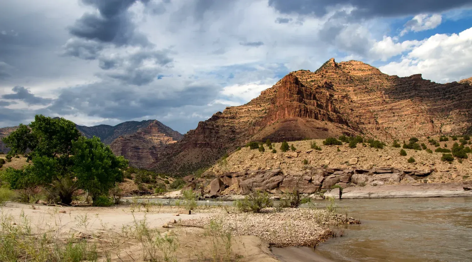 River flowing through a desert landscape with mountains under a cloudy sky.