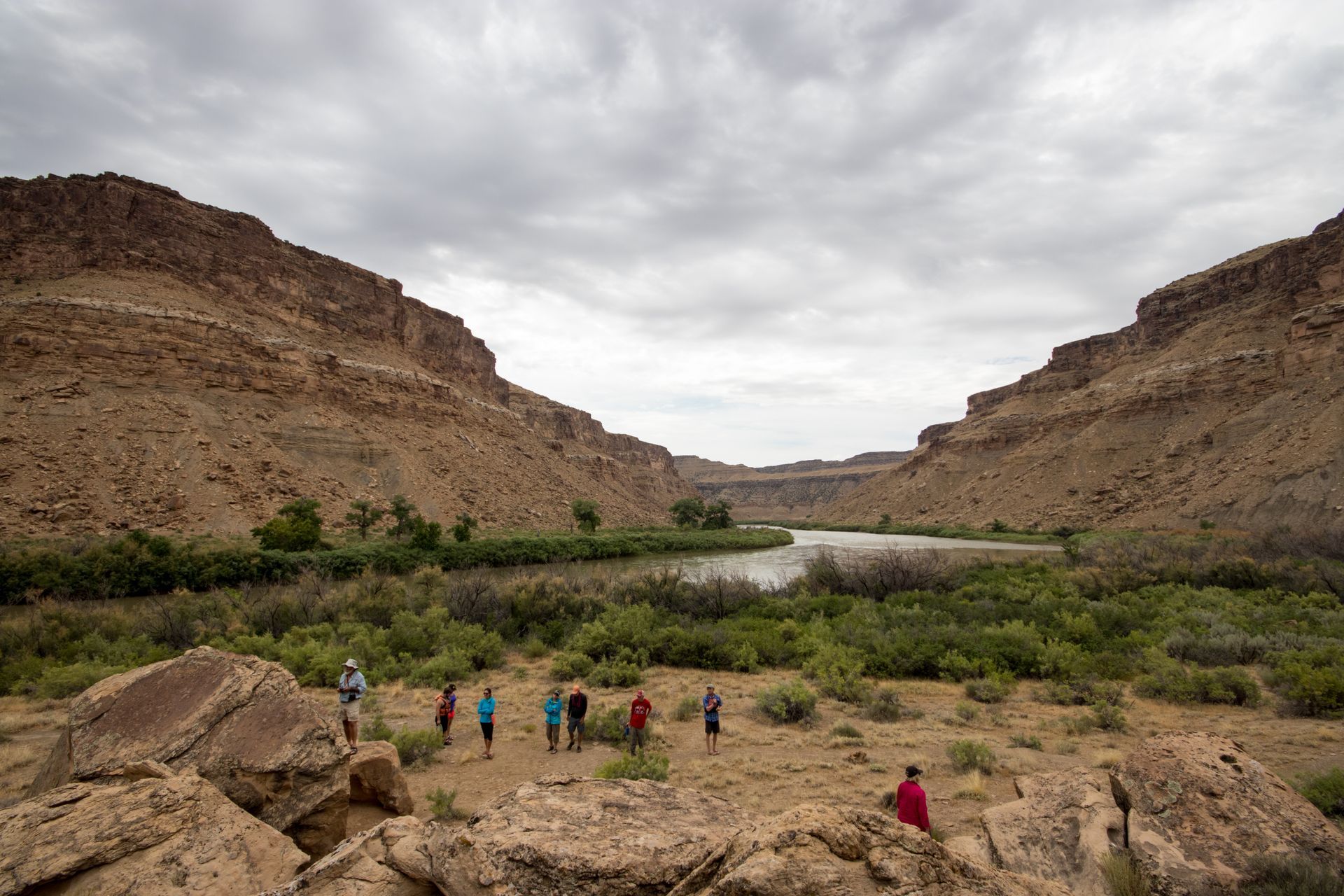 Group of people by a river in a canyon under a cloudy sky.