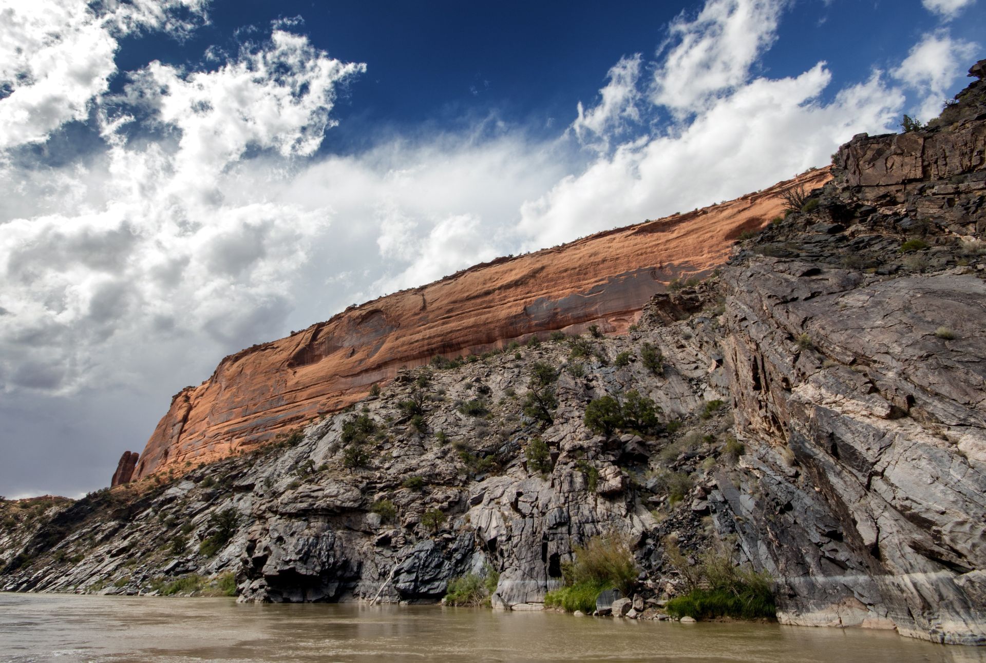 Rocky river landscape with red sandstone cliff and cloudy sky.