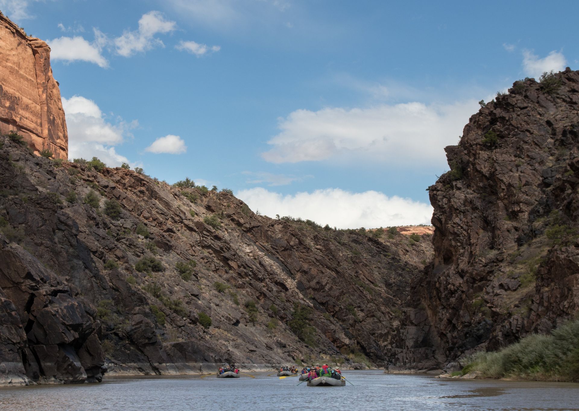Rafting in a river canyon with high rock walls under a partly cloudy sky.