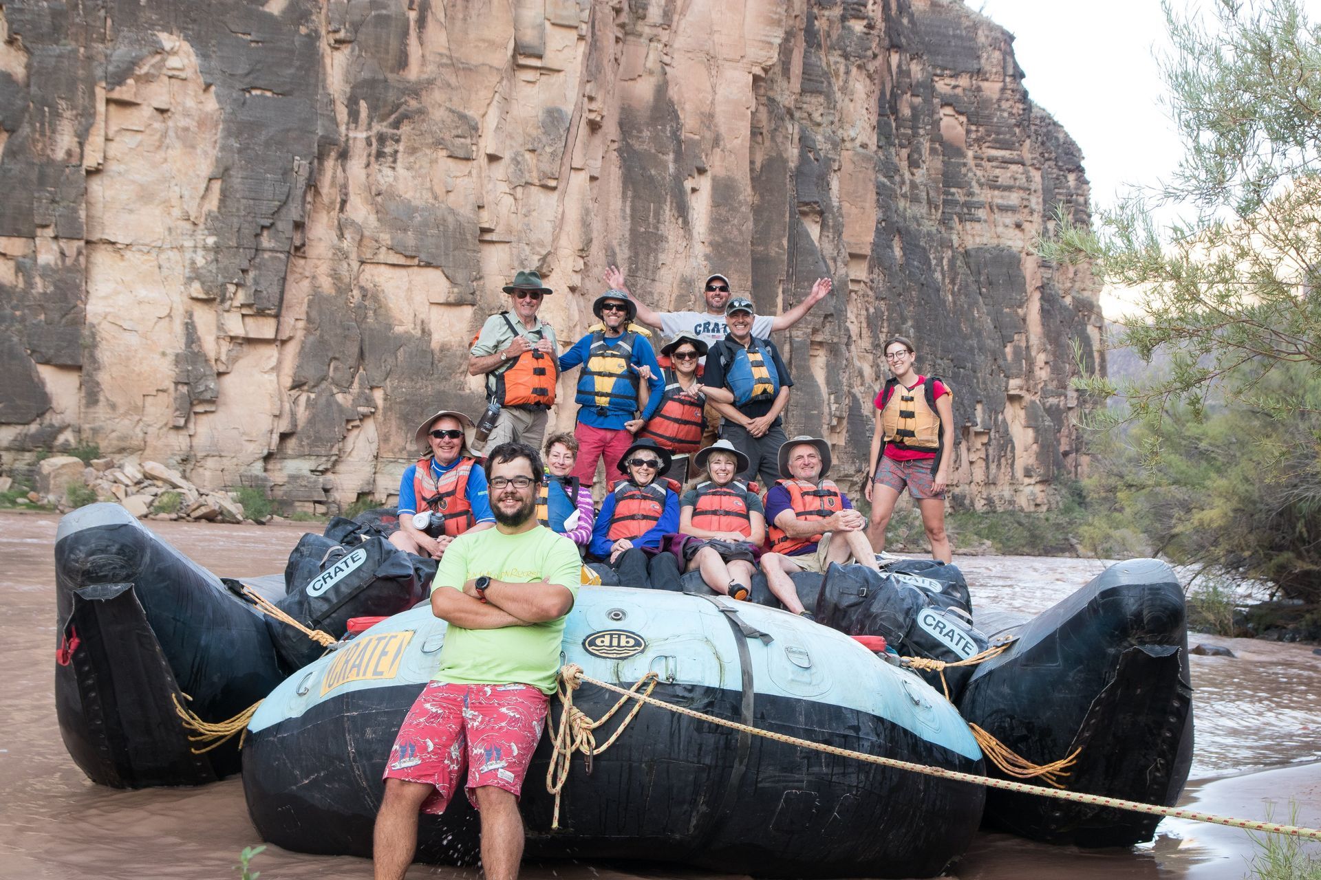 Group of people in life vests on a raft in a canyon, posing for a photo.
