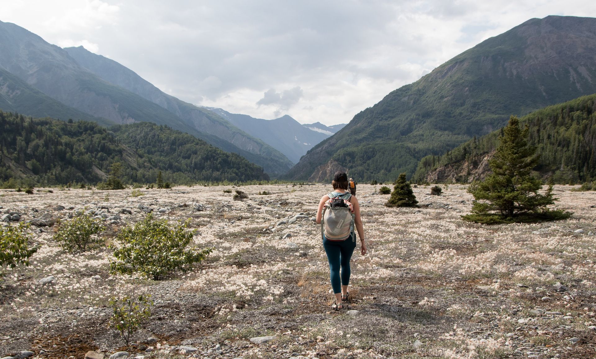 Person hiking through a valley, surrounded by mountains under a cloudy sky.