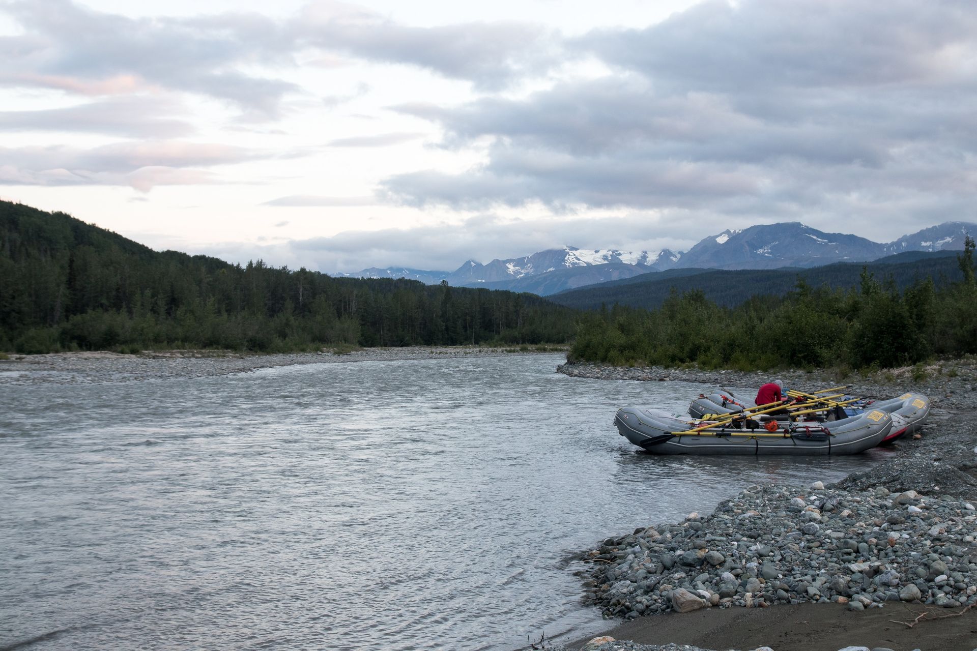 Raft on a riverbank with mountains in the background, under a cloudy sky.