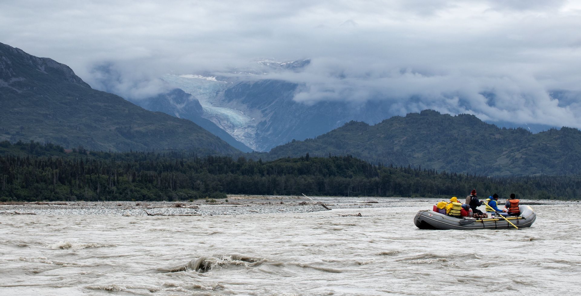 Rafting on a glacial river, mountains in background, cloudy sky.