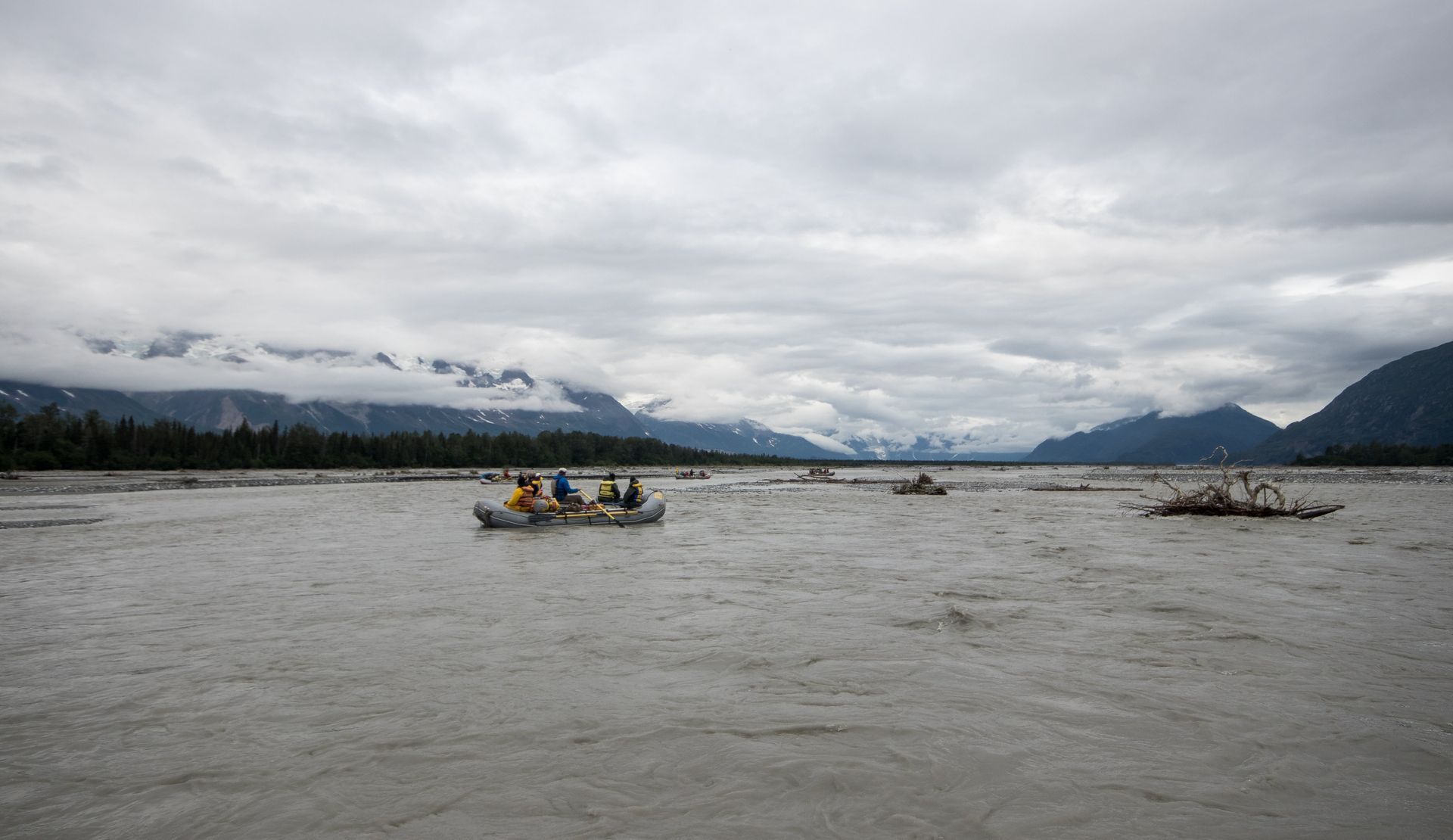 Rafting on a wide, grey river; mountains, overcast sky.