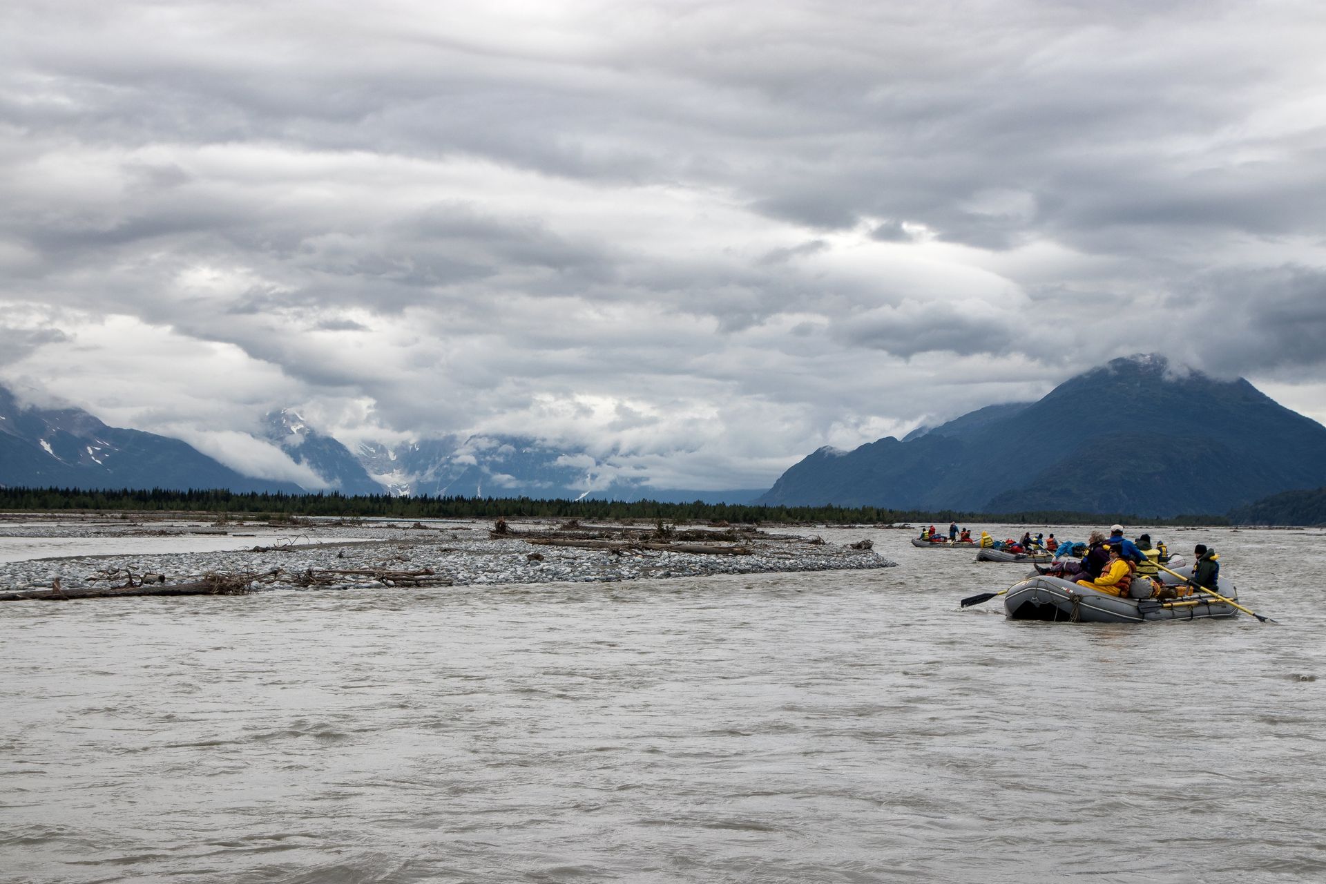 Rafts on a wide, cloudy river. Mountains in the background. Gray sky.