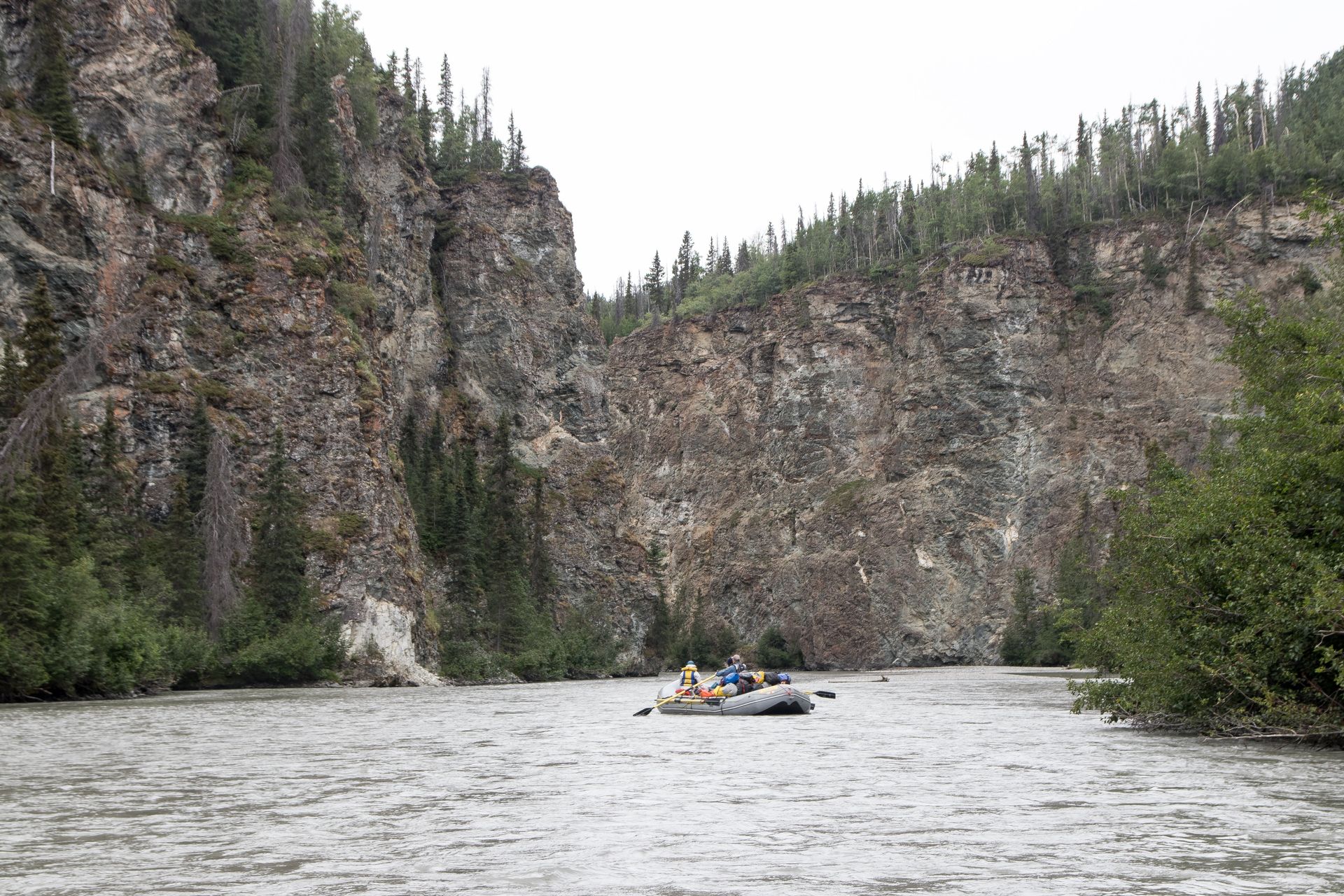 Raft on a river flowing between high rocky cliffs, with trees on top.