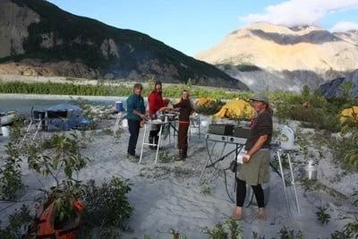 People set up camp in a mountainous, riverside setting.