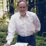 Man in white shirt and jeans standing outside, looking at something off-screen.