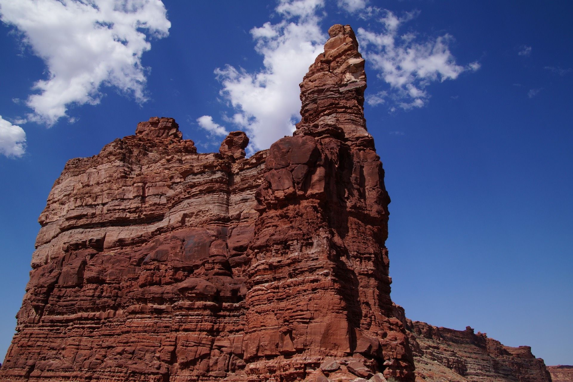 Red rock formation reaching towards a bright blue sky with white clouds.