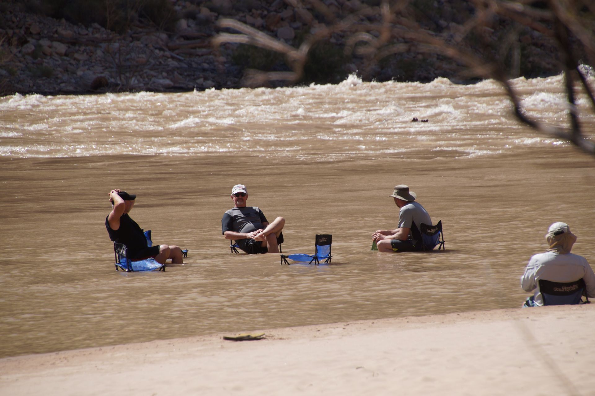 People in camping chairs along a muddy river bank, river in the background.