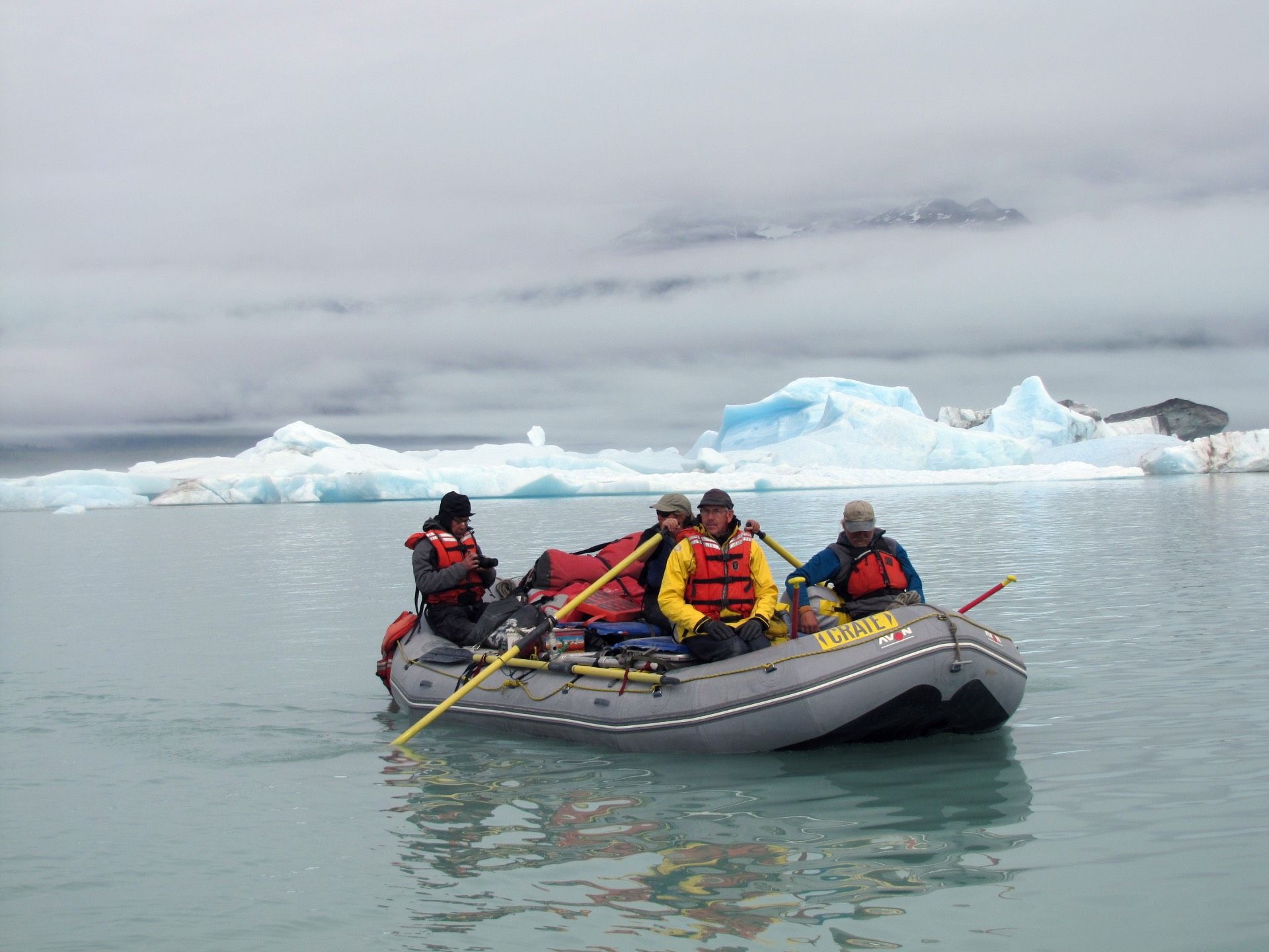 Two people on a raft in a canyon river, wearing life vests and hats.