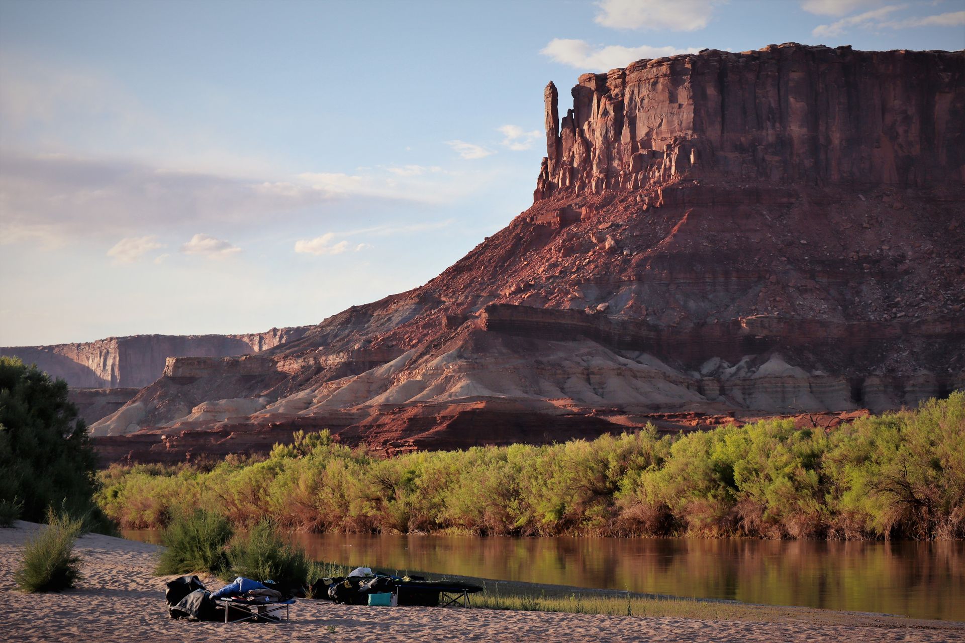 Riverbank scene with large mesa in background; green trees and blue sky.