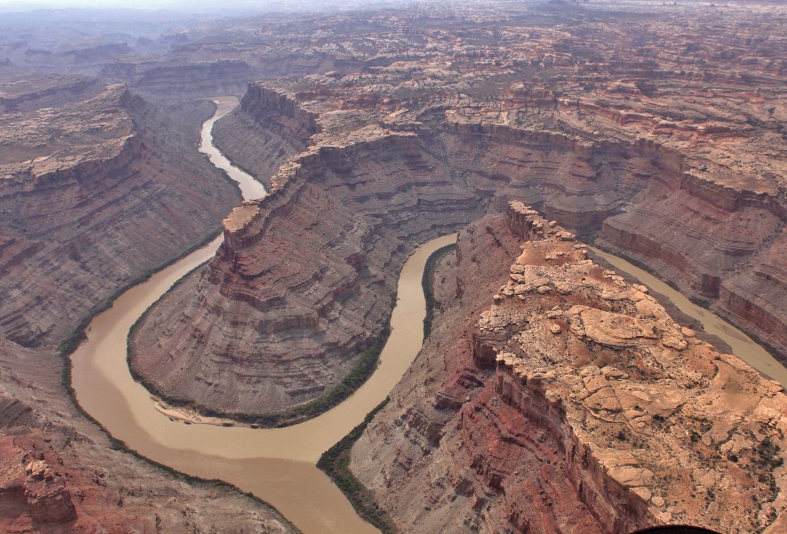 Aerial view of a canyon with a winding river, the landscape is mostly brown and tan.
