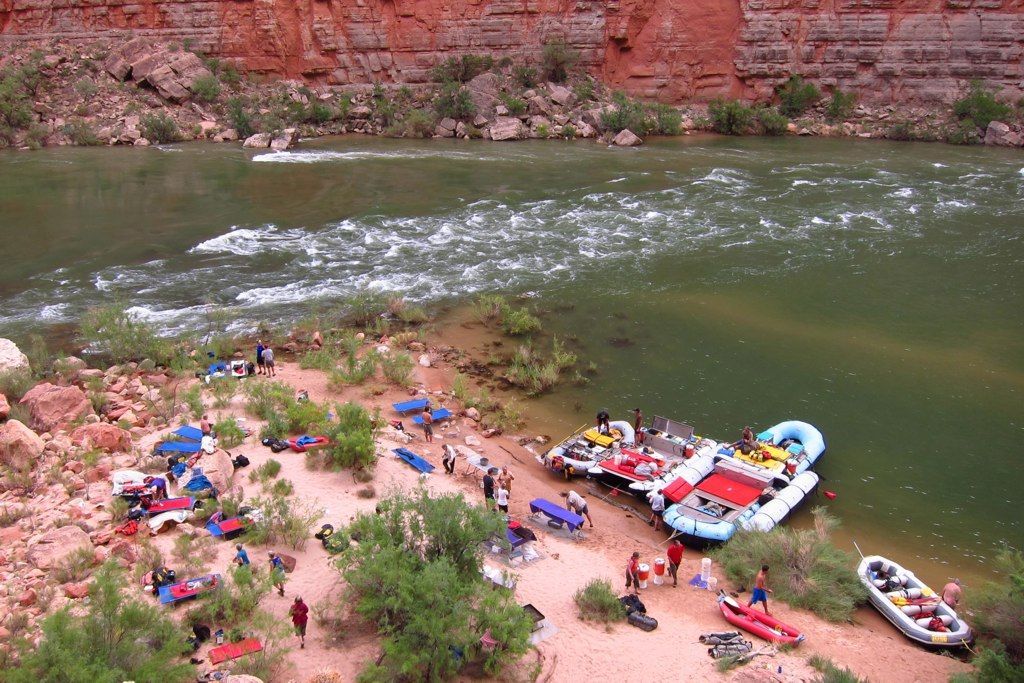 Rafts on a riverbank with people, red rock cliffs in the background.