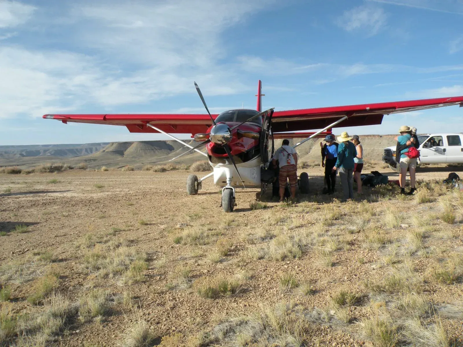 A red and black airplane on a dirt landing strip with people gathered around.