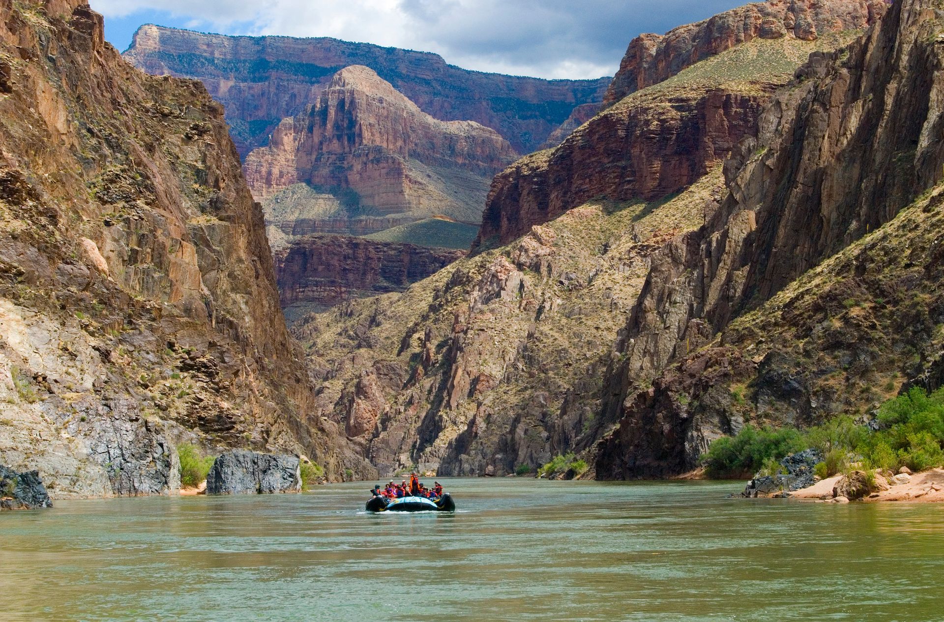 Rafting on a river through the Grand Canyon. Steep, brown canyon walls surround the water.