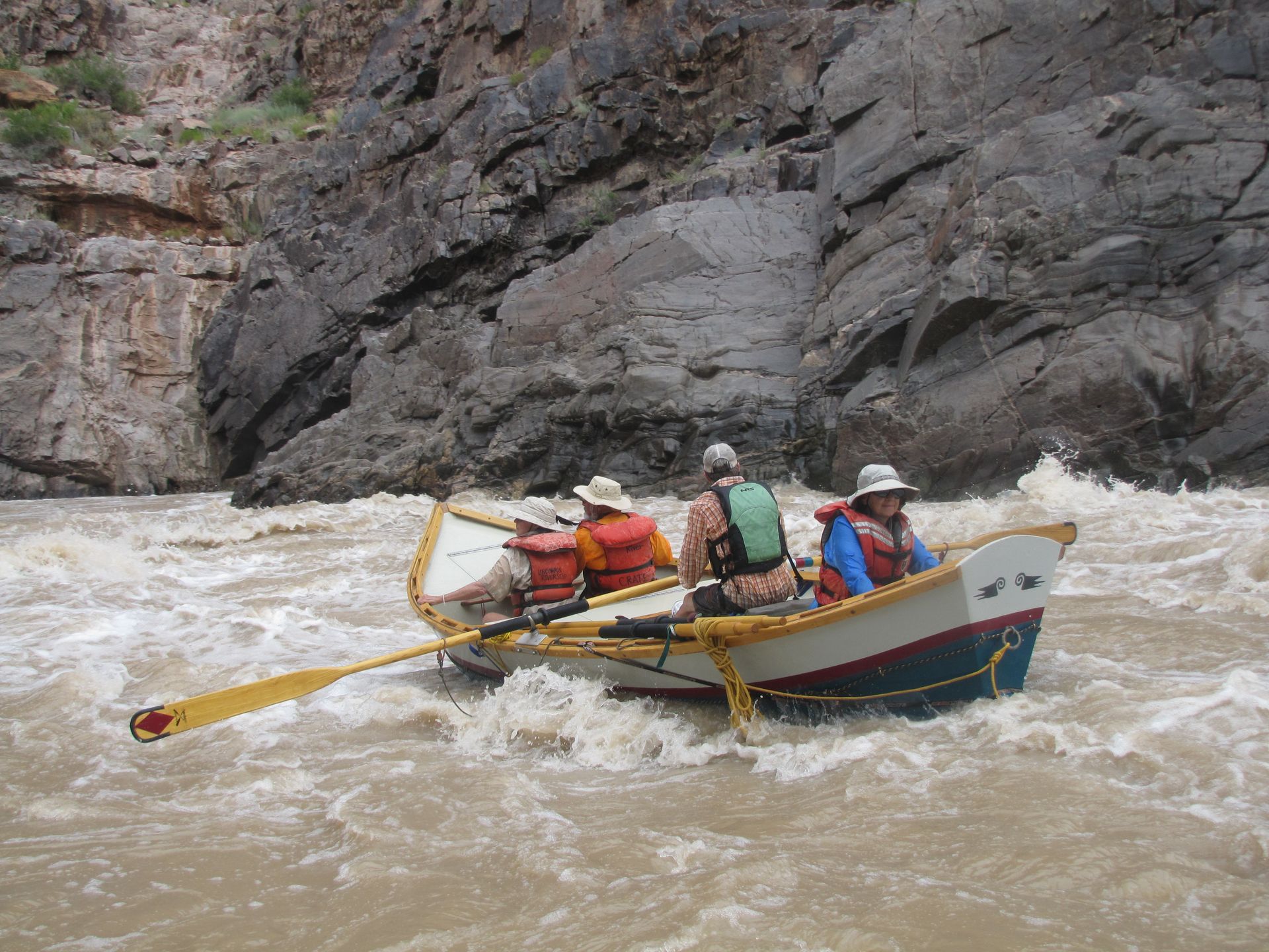 Whitewater rafting boat navigating a rapid; brown water and rocky canyon walls.