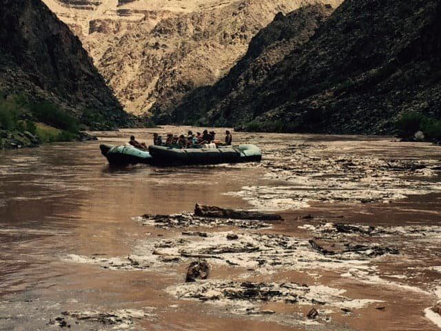 Rafts with people on a muddy river in a canyon.