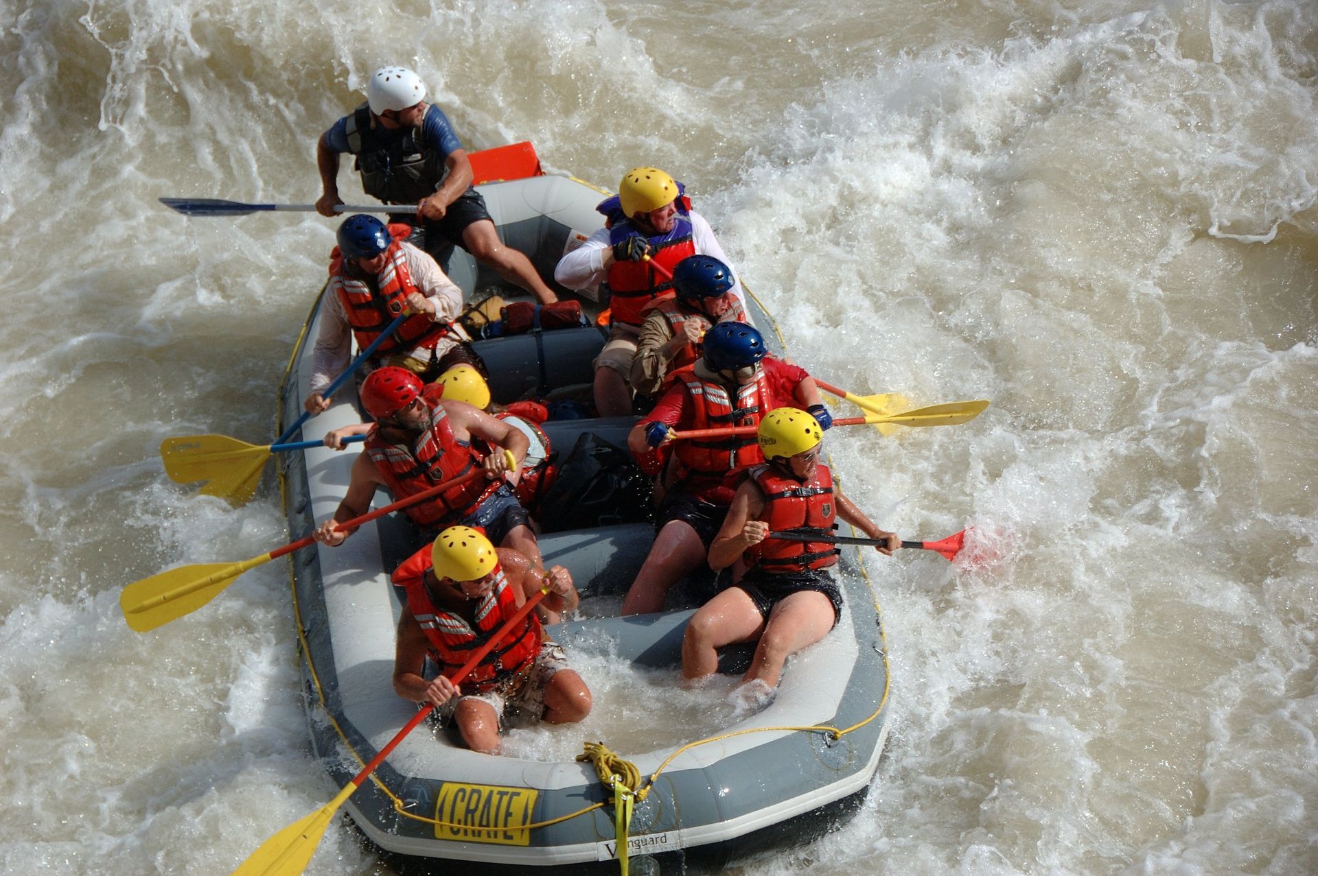 Whitewater rafting, people in a raft navigate choppy, brown water, paddles in action.