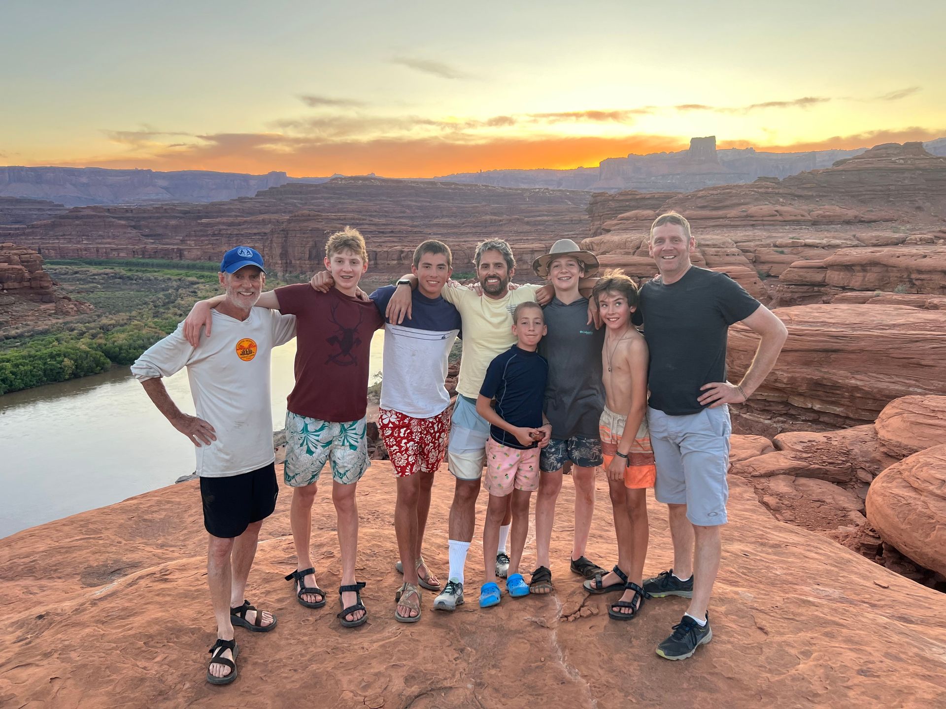 Group of people posing for photo on red rock at sunset, river in background.
