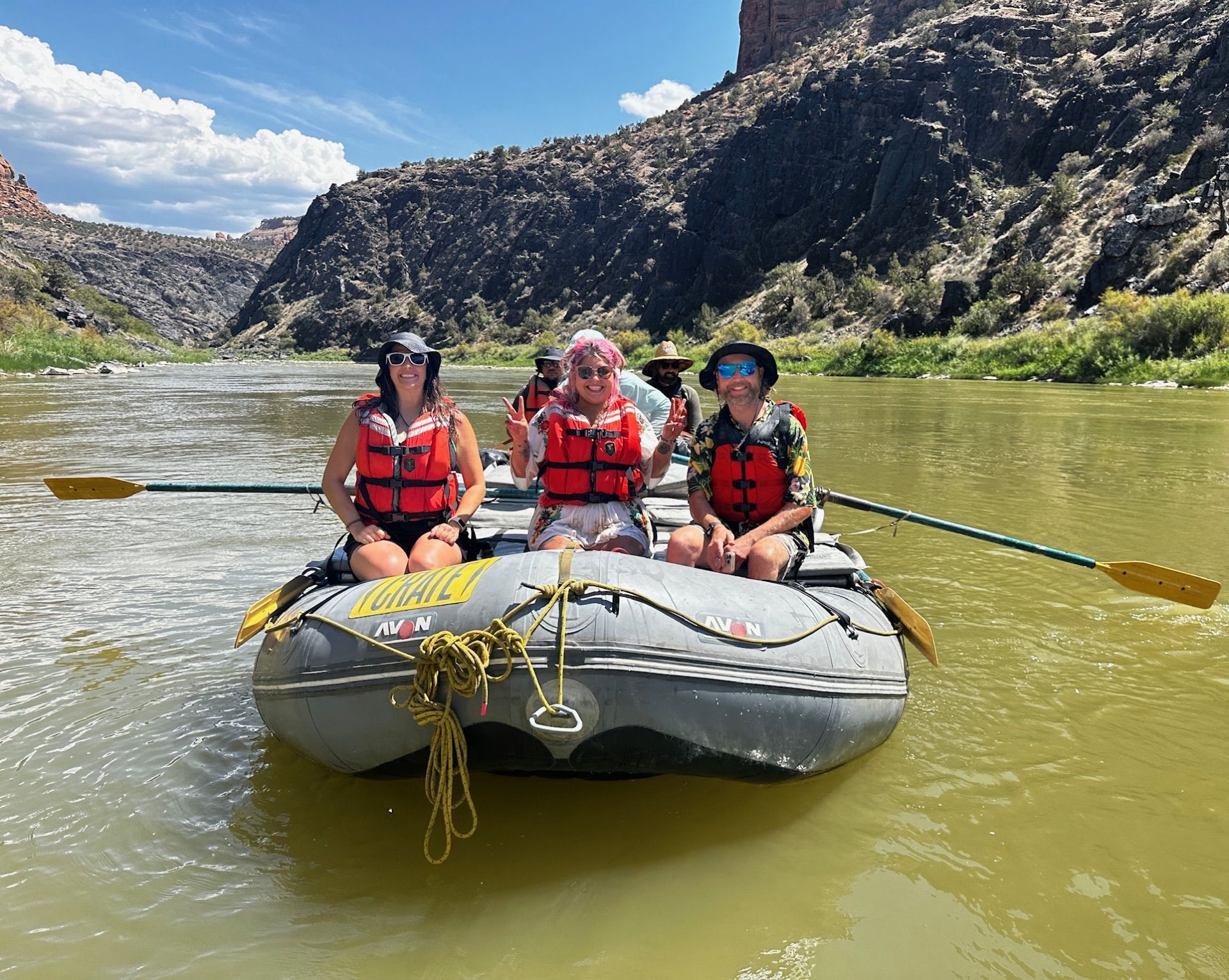 Two people on a raft in a canyon river, wearing life vests and hats.