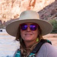 Woman in straw hat and red sunglasses, smiling near a river.