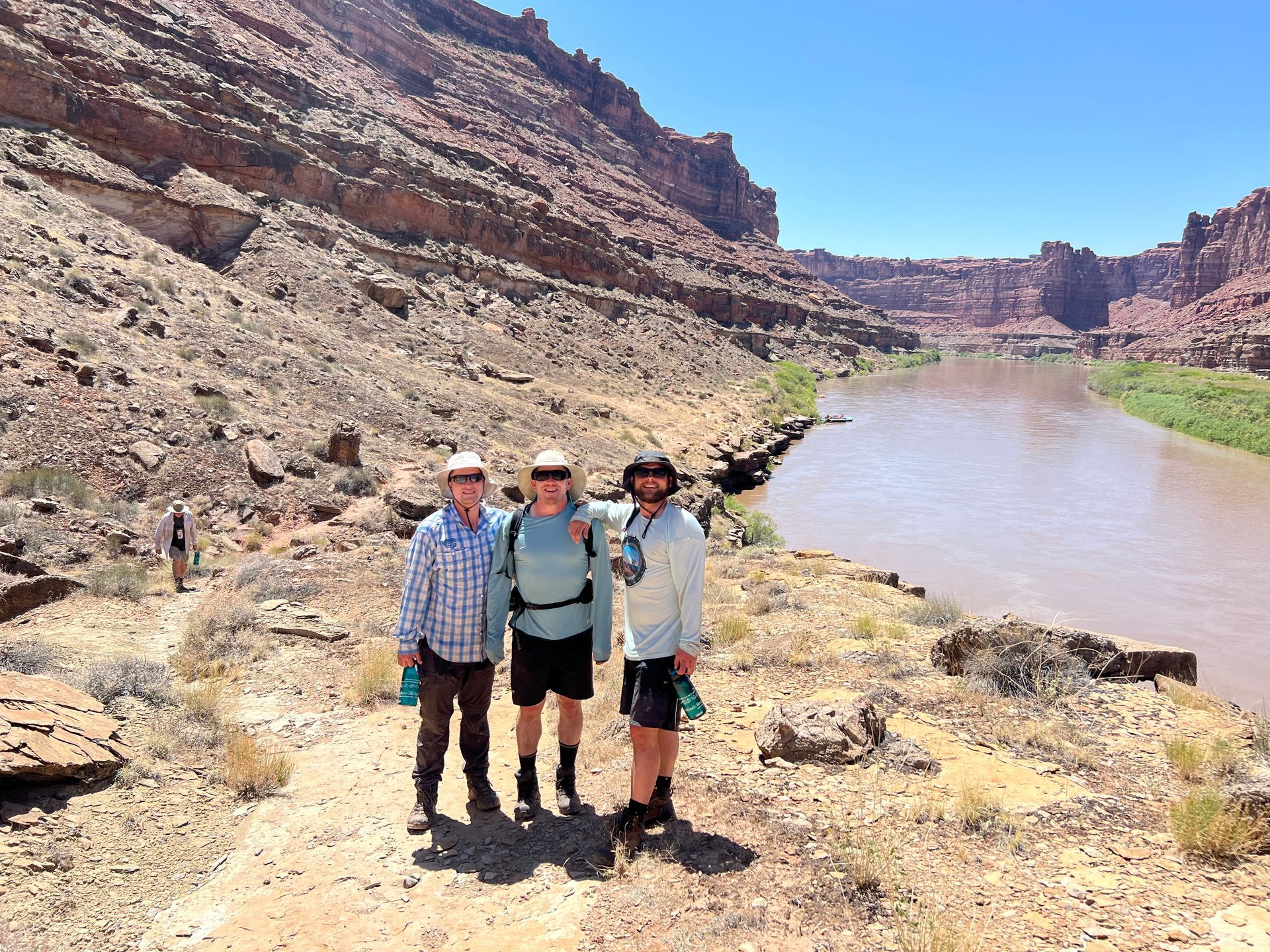 A raft capsizes in a turbulent river, spraying water against a red-brown rock face.