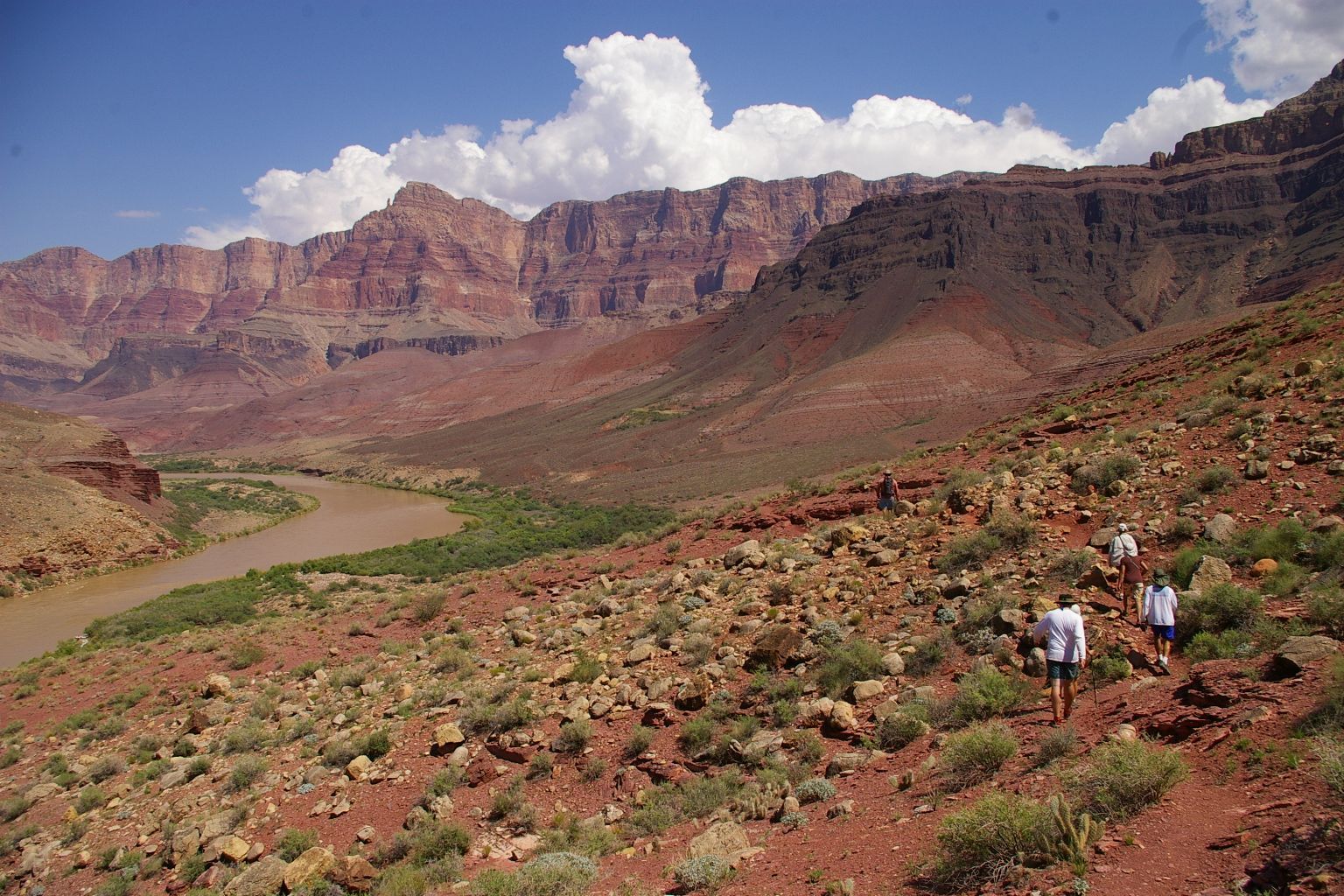Hikers on a red rocky trail overlooking a river in a canyon.