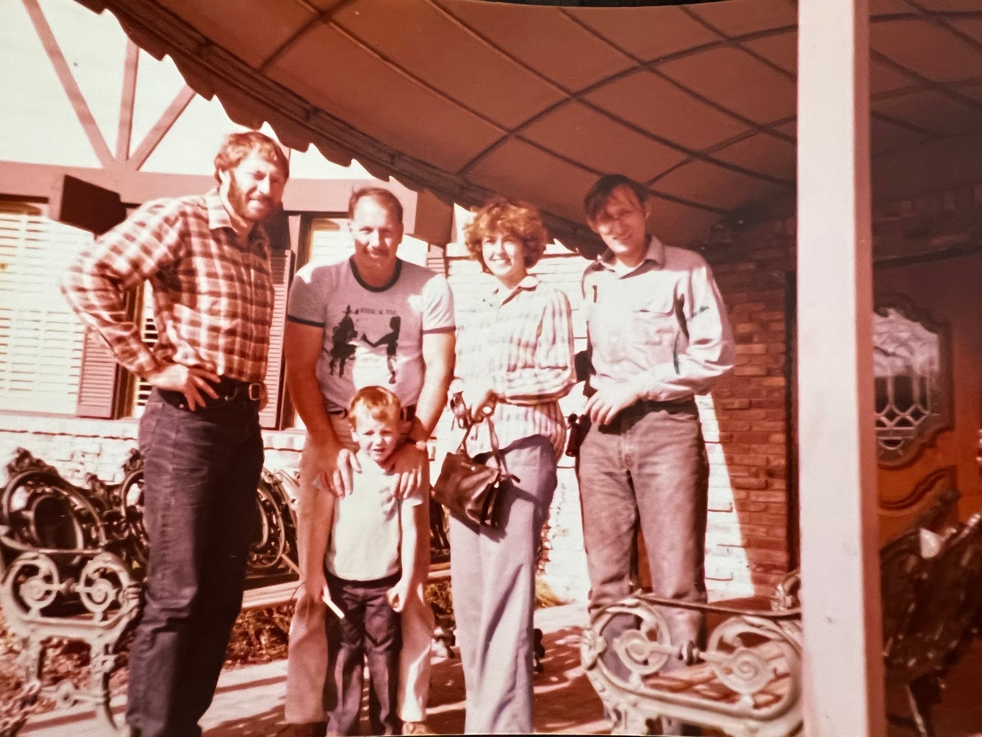 Group of five people posing outdoors, under a roof.  People smiling, some with arms around each other. Vintage photo.