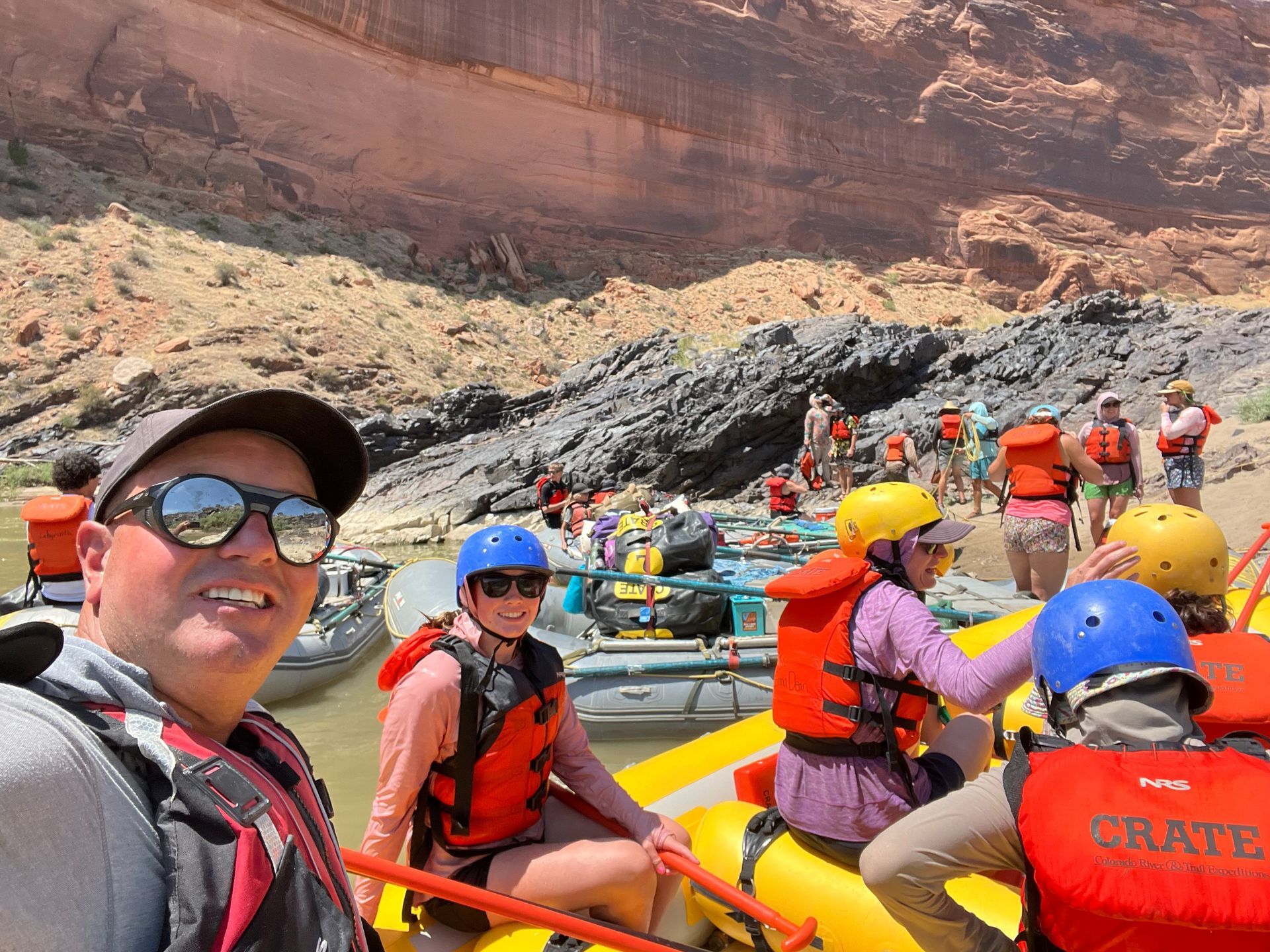 People in life jackets on rafts near a canyon wall, preparing to raft down river.