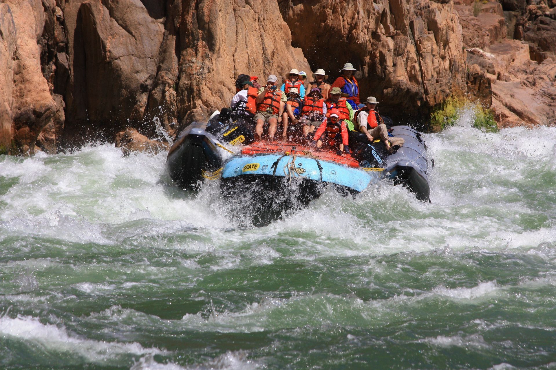 Rafting through whitewater rapids; people in orange life vests are tossed by waves near a canyon.