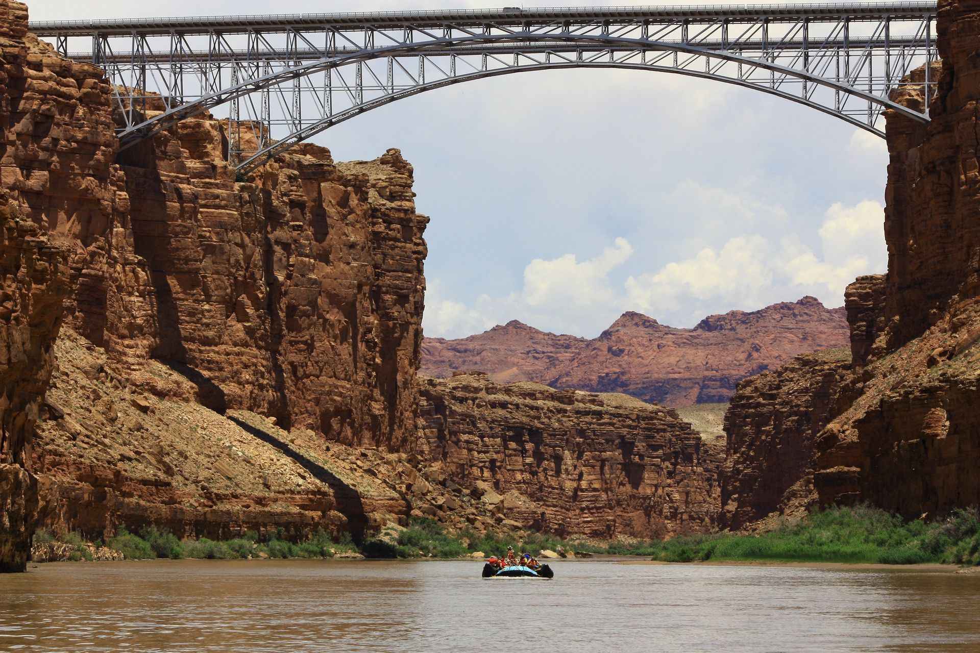 Bridge over a river through a canyon. Boat in the water, red rock cliffs, and blue sky.